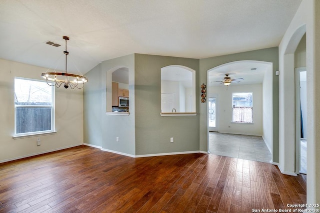 spare room featuring baseboards, visible vents, wood finished floors, and ceiling fan with notable chandelier