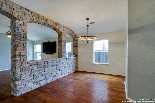 unfurnished dining area with arched walkways, a notable chandelier, wood finished floors, visible vents, and baseboards