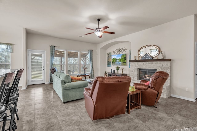 living room with light tile patterned floors, visible vents, baseboards, ceiling fan, and a stone fireplace