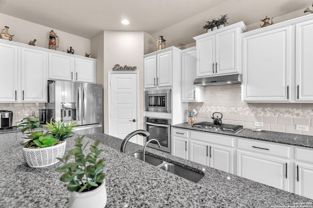 kitchen with appliances with stainless steel finishes, white cabinets, a sink, dark stone counters, and under cabinet range hood