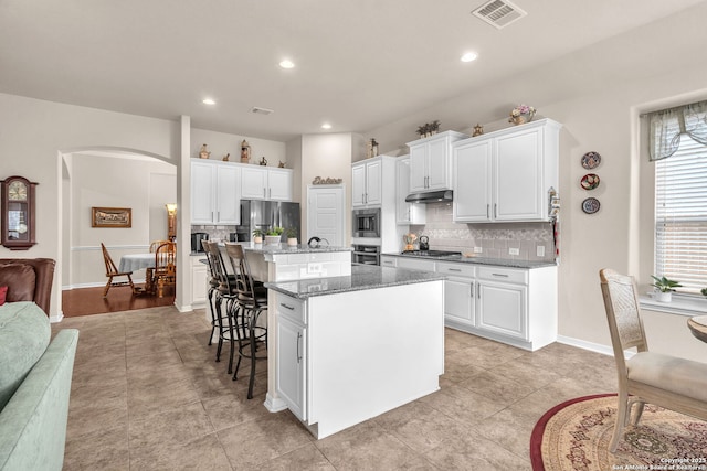 kitchen featuring a breakfast bar area, stainless steel appliances, visible vents, white cabinets, and a center island with sink