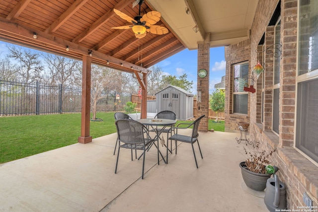 view of patio / terrace with a storage shed, a fenced backyard, ceiling fan, an outbuilding, and outdoor dining space