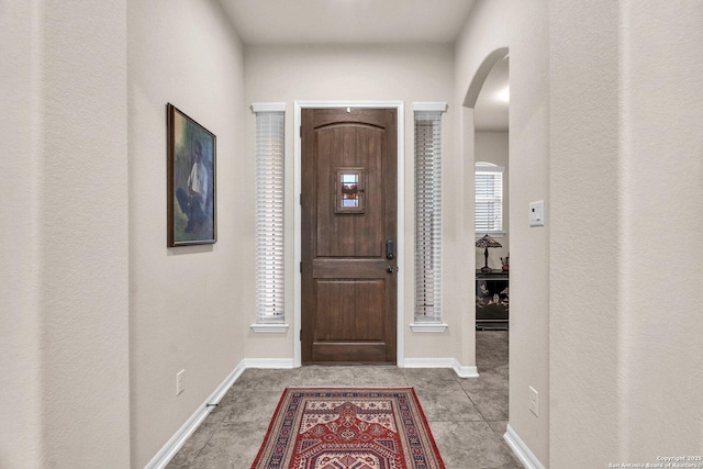 foyer entrance featuring arched walkways, baseboards, and light tile patterned floors