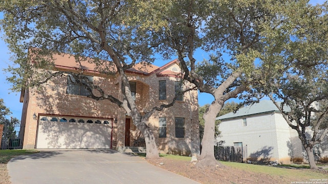 traditional-style home featuring a garage, driveway, brick siding, and fence