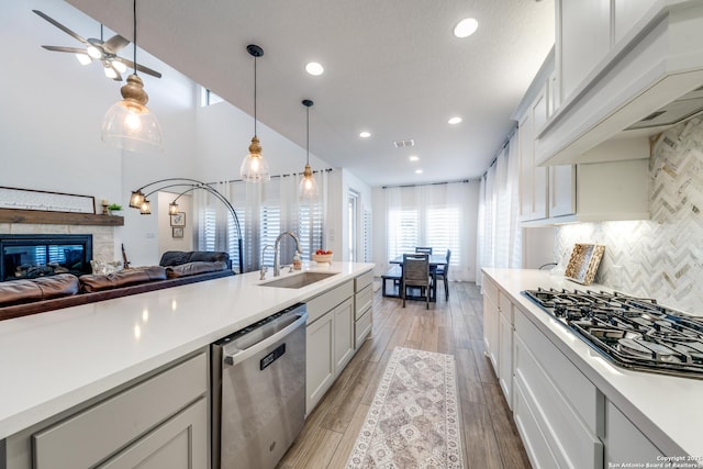 kitchen with light countertops, appliances with stainless steel finishes, open floor plan, a sink, and premium range hood