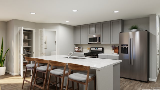 kitchen featuring a kitchen island with sink, wood finished floors, a sink, appliances with stainless steel finishes, and gray cabinets