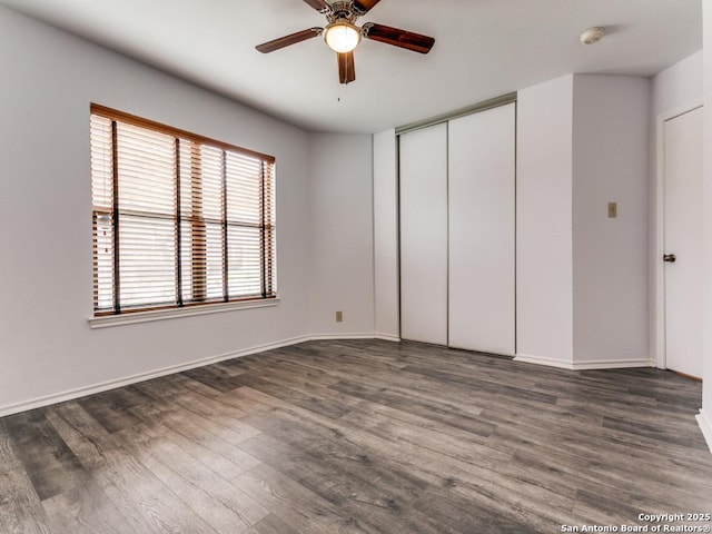 unfurnished bedroom with dark wood-style floors, ceiling fan, a closet, and baseboards