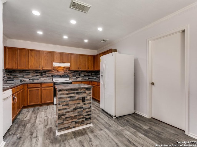 kitchen featuring dark countertops, ornamental molding, wood finished floors, white appliances, and under cabinet range hood