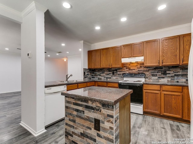 kitchen with under cabinet range hood, white appliances, a sink, a kitchen island, and dark countertops