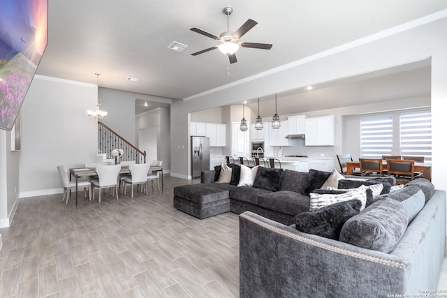 living area with visible vents, light wood-style flooring, ornamental molding, baseboards, and ceiling fan with notable chandelier