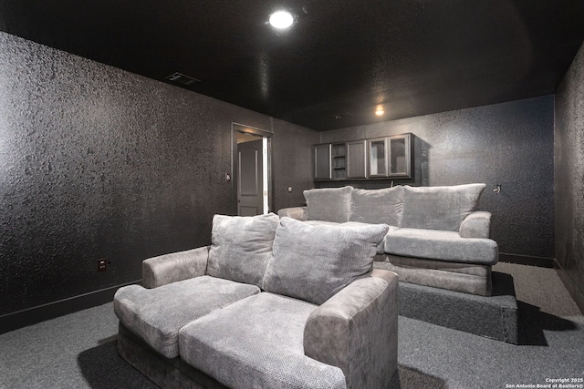 carpeted cinema room featuring visible vents and a textured wall