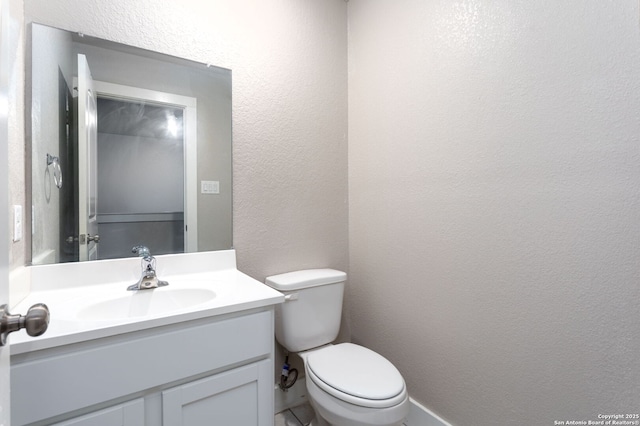 half bath featuring toilet, vanity, and a textured wall