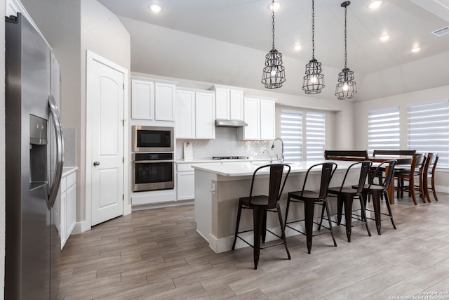 kitchen featuring light countertops, hanging light fixtures, appliances with stainless steel finishes, a kitchen island with sink, and white cabinetry