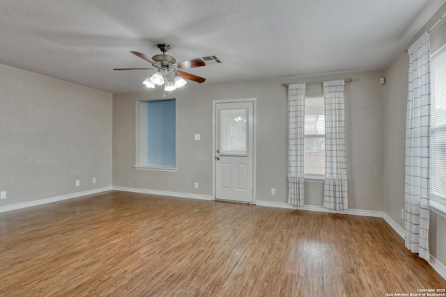 spare room featuring a textured ceiling, light wood-style flooring, visible vents, baseboards, and a ceiling fan