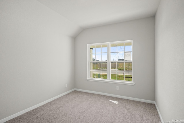 carpeted empty room featuring baseboards and vaulted ceiling