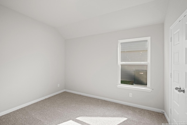 carpeted empty room featuring vaulted ceiling and baseboards