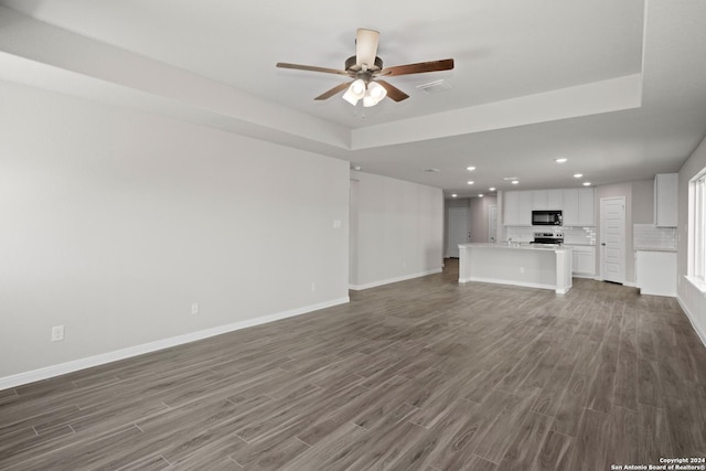 unfurnished living room with dark wood-style flooring, a raised ceiling, and baseboards