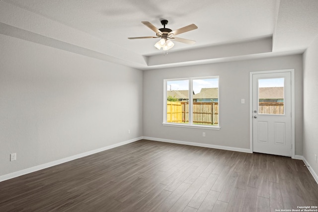 spare room featuring a ceiling fan, a tray ceiling, dark wood-style flooring, and baseboards