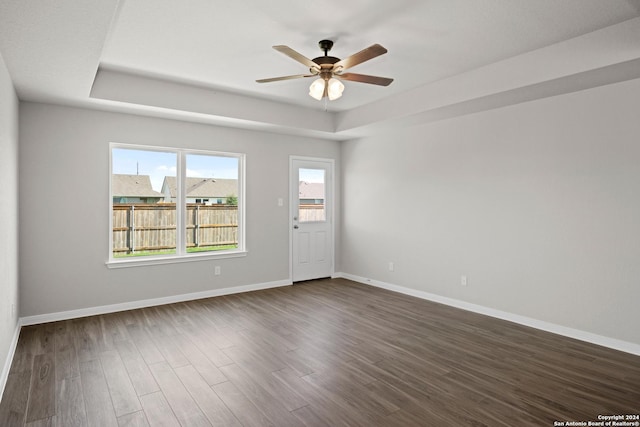 unfurnished room with dark wood-style floors, baseboards, a tray ceiling, and ceiling fan