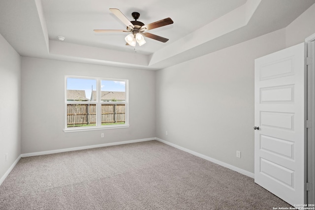 unfurnished room with a raised ceiling, carpet flooring, ceiling fan, and baseboards