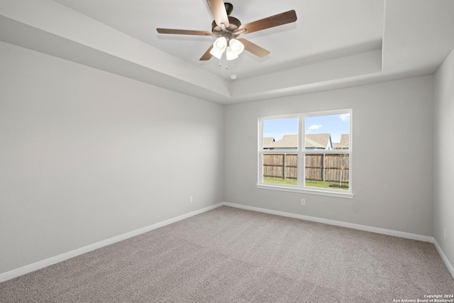 carpeted empty room featuring baseboards, a tray ceiling, and ceiling fan