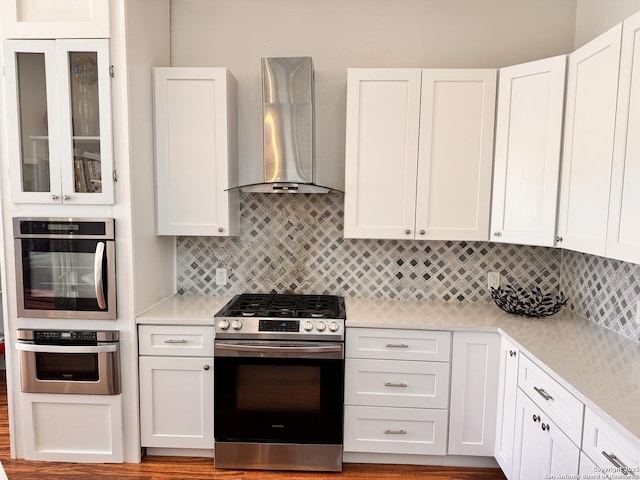 kitchen featuring appliances with stainless steel finishes, white cabinets, light countertops, and wall chimney range hood