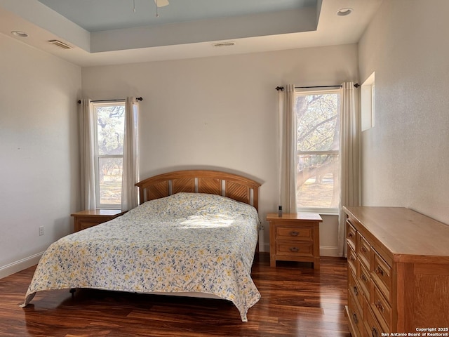 bedroom with dark wood-style floors, a raised ceiling, multiple windows, and baseboards