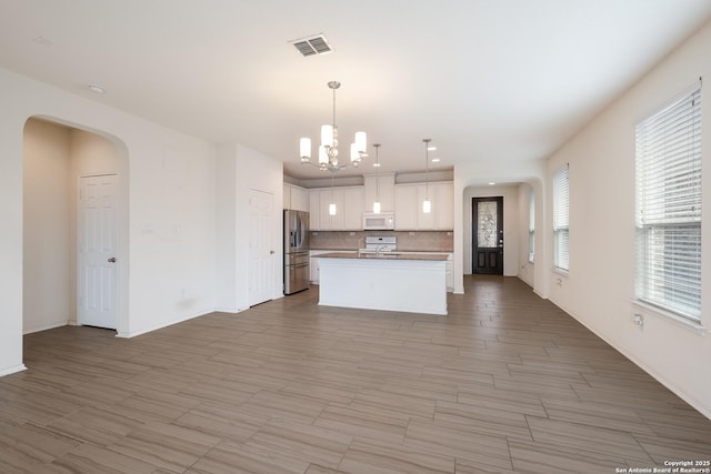 kitchen featuring white appliances, visible vents, white cabinets, a kitchen island, and pendant lighting