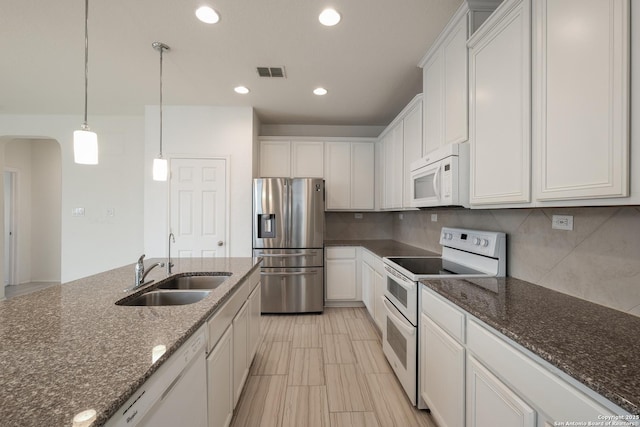 kitchen with white appliances, white cabinetry, a sink, and dark stone countertops