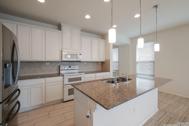 kitchen with white appliances, a sink, white cabinets, a center island with sink, and decorative light fixtures