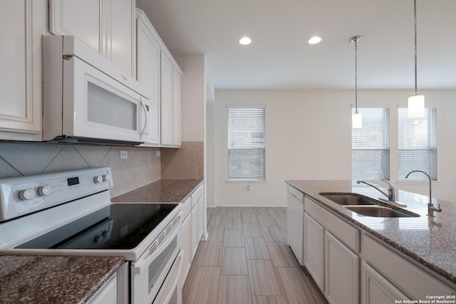 kitchen with white appliances, decorative backsplash, white cabinets, pendant lighting, and a sink