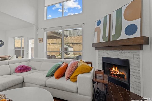 living room featuring a towering ceiling, a stone fireplace, wood finished floors, and a wealth of natural light