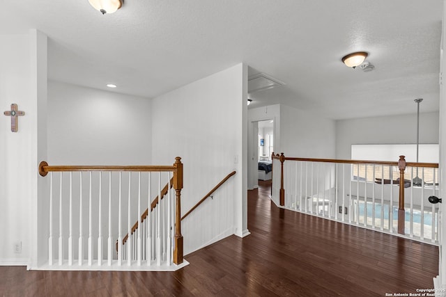 corridor with a textured ceiling, wood finished floors, an upstairs landing, and attic access