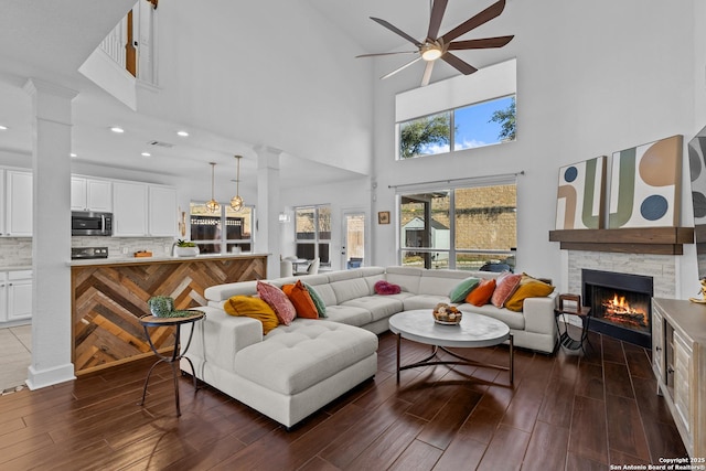 living area with a ceiling fan, dark wood-style flooring, a stone fireplace, and ornate columns