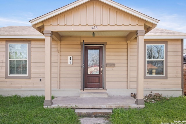 view of exterior entry with board and batten siding, covered porch, and a shingled roof