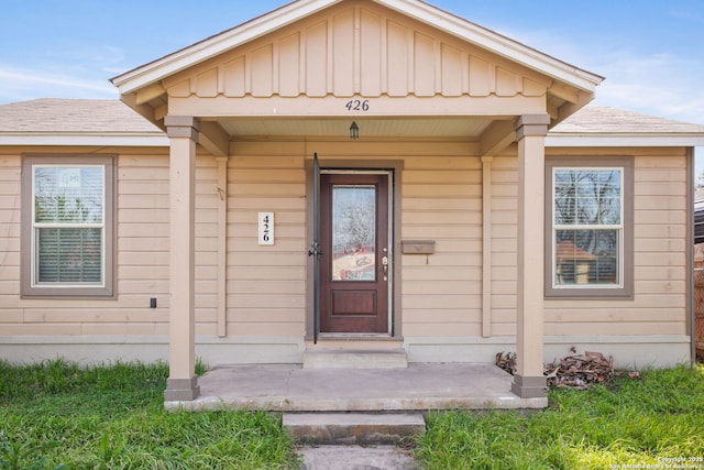 entrance to property featuring covered porch, a shingled roof, and board and batten siding