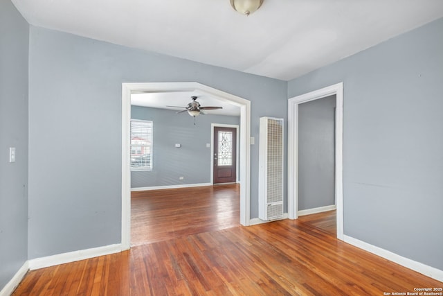 unfurnished room with ceiling fan, baseboards, wood finished floors, and a heating unit