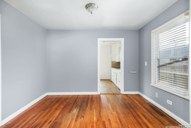 unfurnished bedroom with ensuite bathroom, dark wood-type flooring, and baseboards