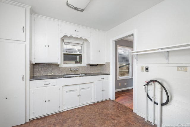 kitchen with dark countertops, a healthy amount of sunlight, white cabinetry, and a sink