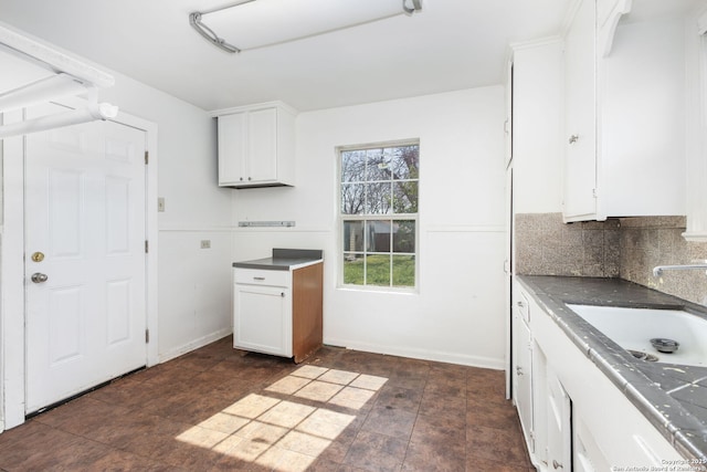 kitchen featuring baseboards, dark countertops, a sink, white cabinetry, and backsplash