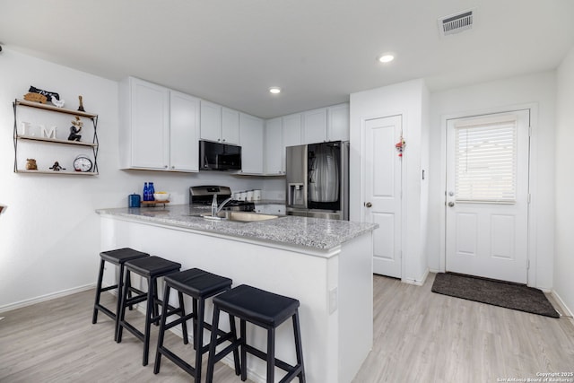 kitchen featuring stainless steel appliances, a breakfast bar, a peninsula, visible vents, and white cabinets