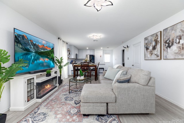 living area with a glass covered fireplace, light wood-style flooring, and baseboards