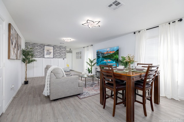 dining area with light wood-type flooring, a wainscoted wall, visible vents, and baseboards