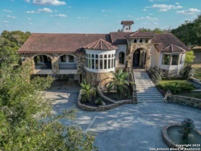 mediterranean / spanish home with stone siding, stairs, aphalt driveway, and a tiled roof