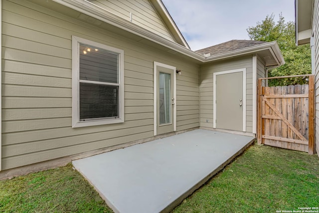 view of exterior entry featuring a lawn, a patio area, fence, and a gate