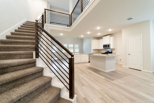 staircase featuring visible vents, baseboards, wood finished floors, a high ceiling, and recessed lighting