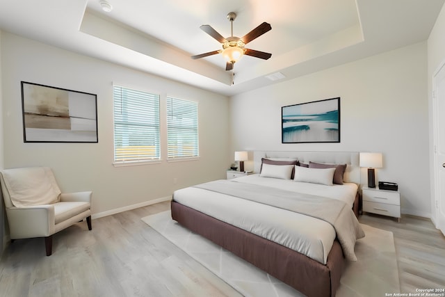 bedroom featuring visible vents, a tray ceiling, light wood-style flooring, and baseboards