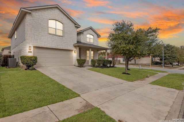 view of front facade featuring a garage, central AC unit, concrete driveway, stone siding, and a yard