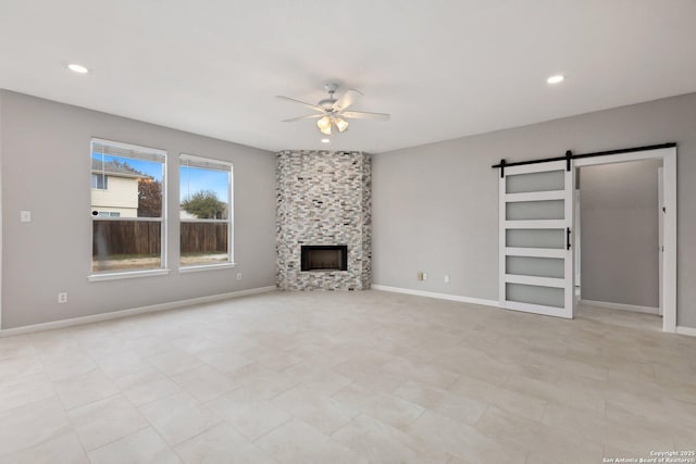 unfurnished living room with a fireplace, recessed lighting, a barn door, ceiling fan, and baseboards