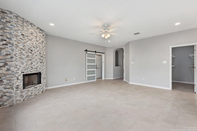 unfurnished living room with arched walkways, ceiling fan, a barn door, a stone fireplace, and visible vents